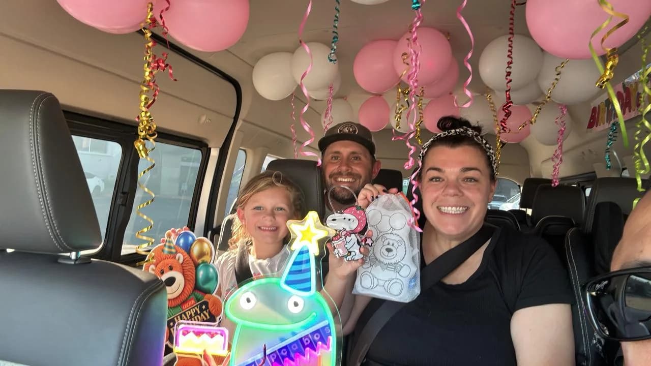 A father, mother and their daughter smiling together inside a van full of balloons and streamers