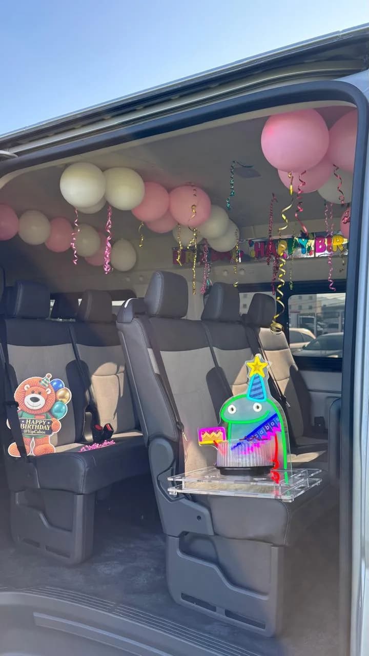 A VIP Transportation van at the airport, decorated with pink and white balloons, streamers and a Happy Birthday banner, with a Goleón birthday sign, a glowing sign and a cake on a tray, waiting for the guests