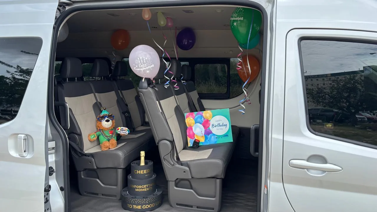A van decorated for a birthday, with balloons, a card and Goleón in a seat