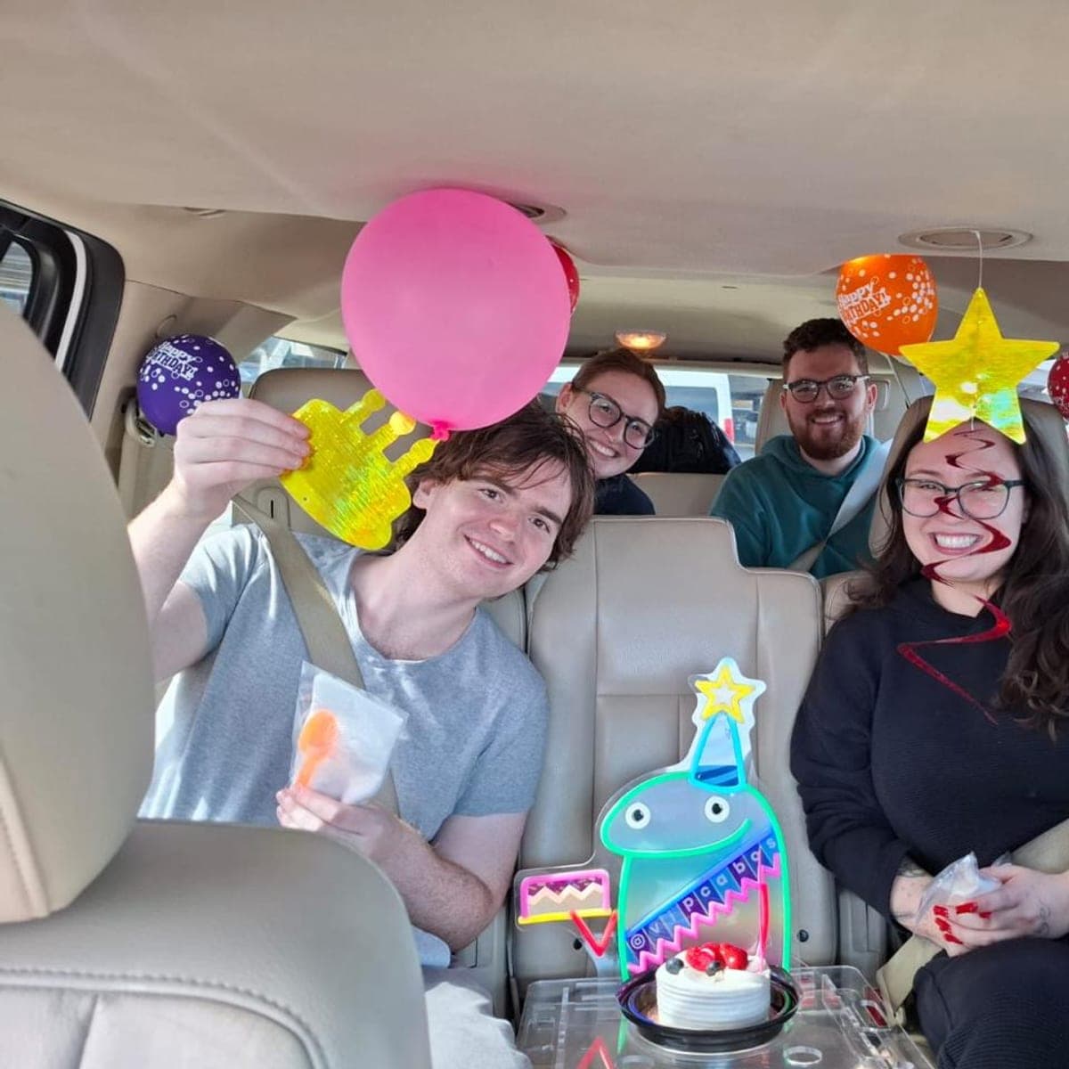 Birthday group in the van with cake, balloons and party signs